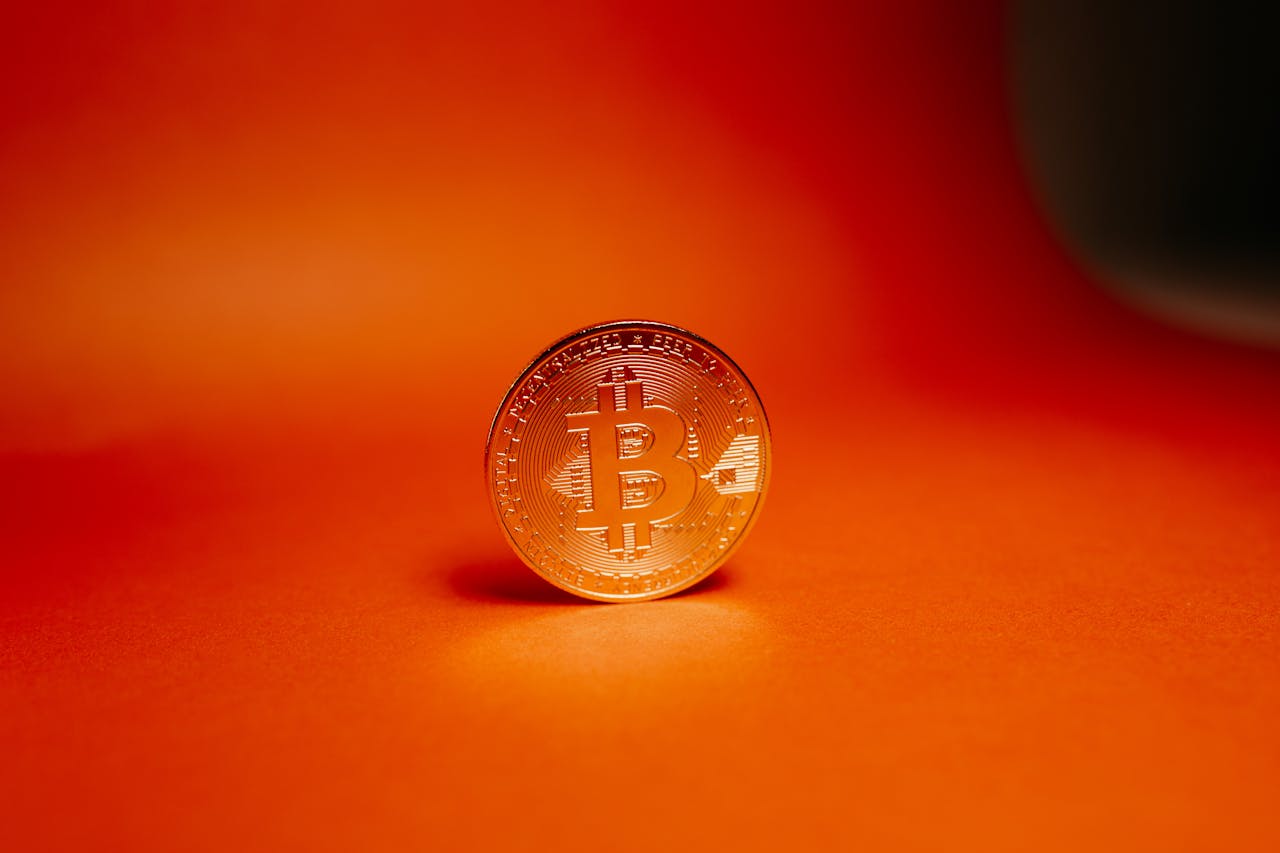 gallery-01 Close-up of a gold Bitcoin coin on a bright orange background, representing cryptocurrency.